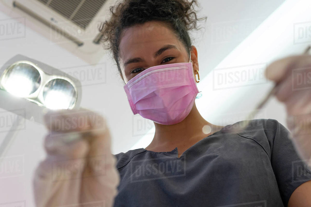 Low angle closeup of ethnic female doctor using dental explorer and cleaning teeth of patient in