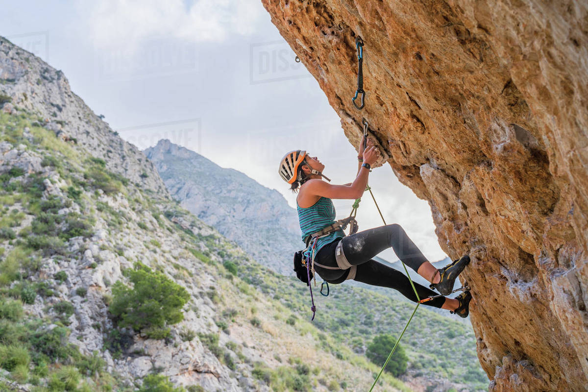 From below side view of active focused youthful female alpinist climbing on cliff in summer day Royalty-free stock photo