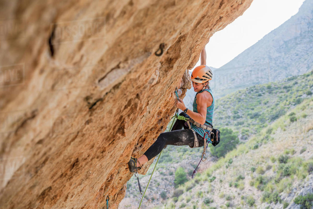 From below side view of active focused youthful female alpinist climbing on cliff in summer day Royalty-free stock photo