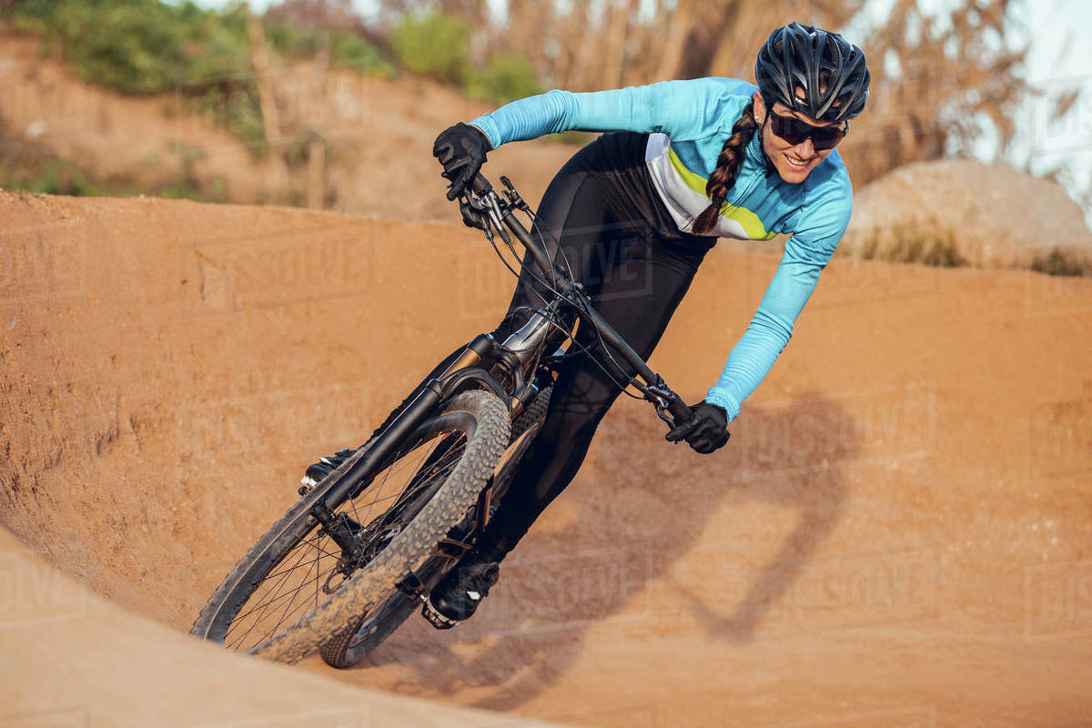 Sportswoman in black helmet and blue sportswear with glasses riding mountain bike on training track Royalty-free stock photo