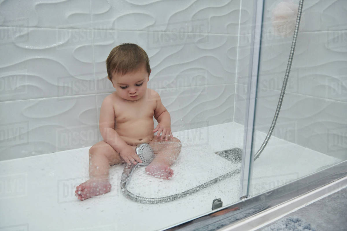 Cute little toddler sitting on floor of shower cabin and enjoying water
