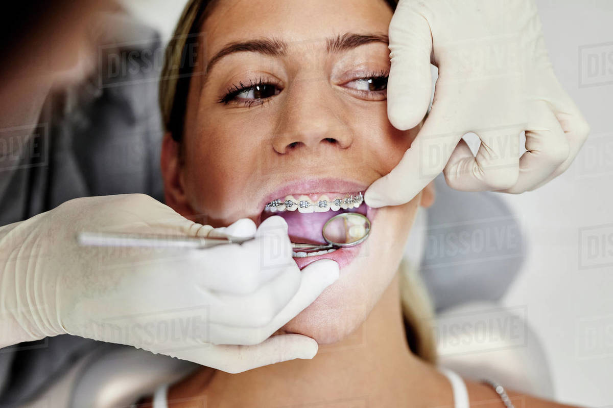 From above crop female dentist in gloves using mirror to check teeth of