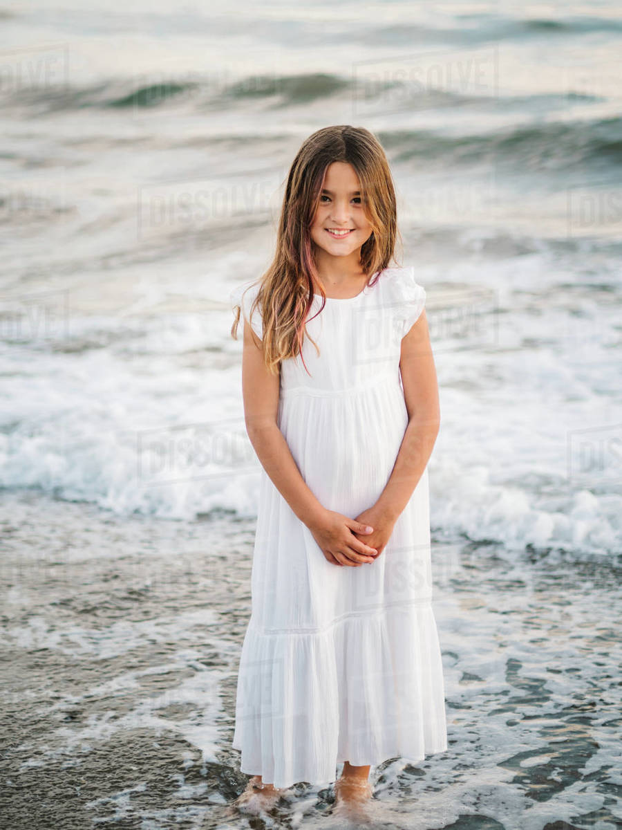 Portrait of charming little girl in white dress standing in water