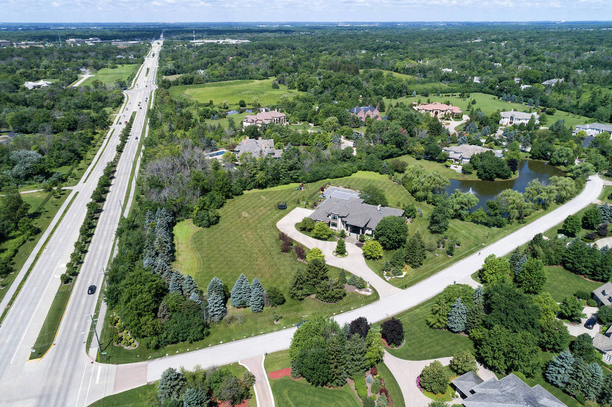 Aerial view of a luxury neighborhood with mature trees and a pond in a Chicago suburban