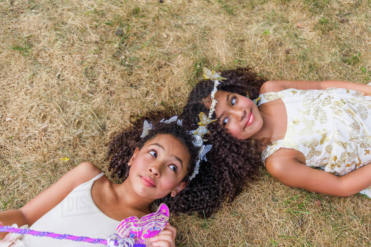 Two young girls, dressed as fairies, lying on grass, touching heads Royalty-free stock photo