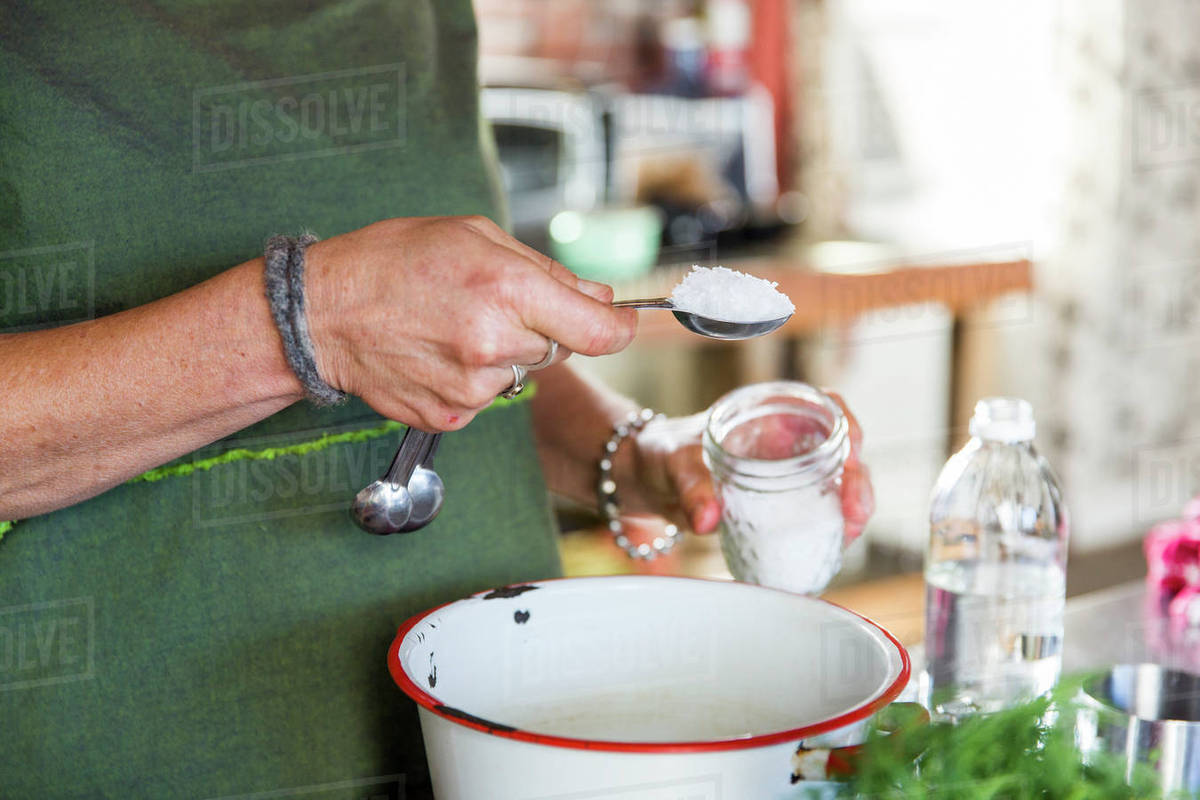 Hand of woman adding sea salt to bowl in kitchen Stock Photo Dissolve