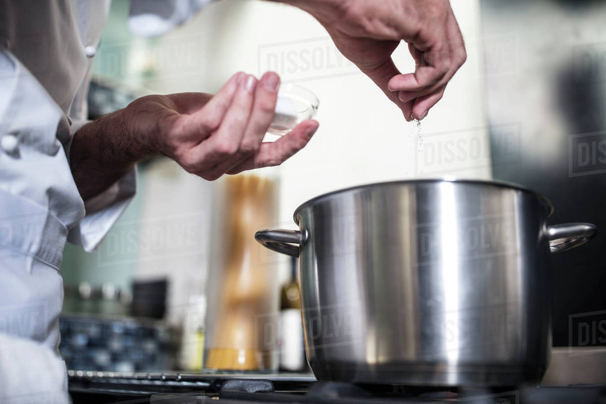 Chef putting salt in pan of water on stove, closeup Stock Photo