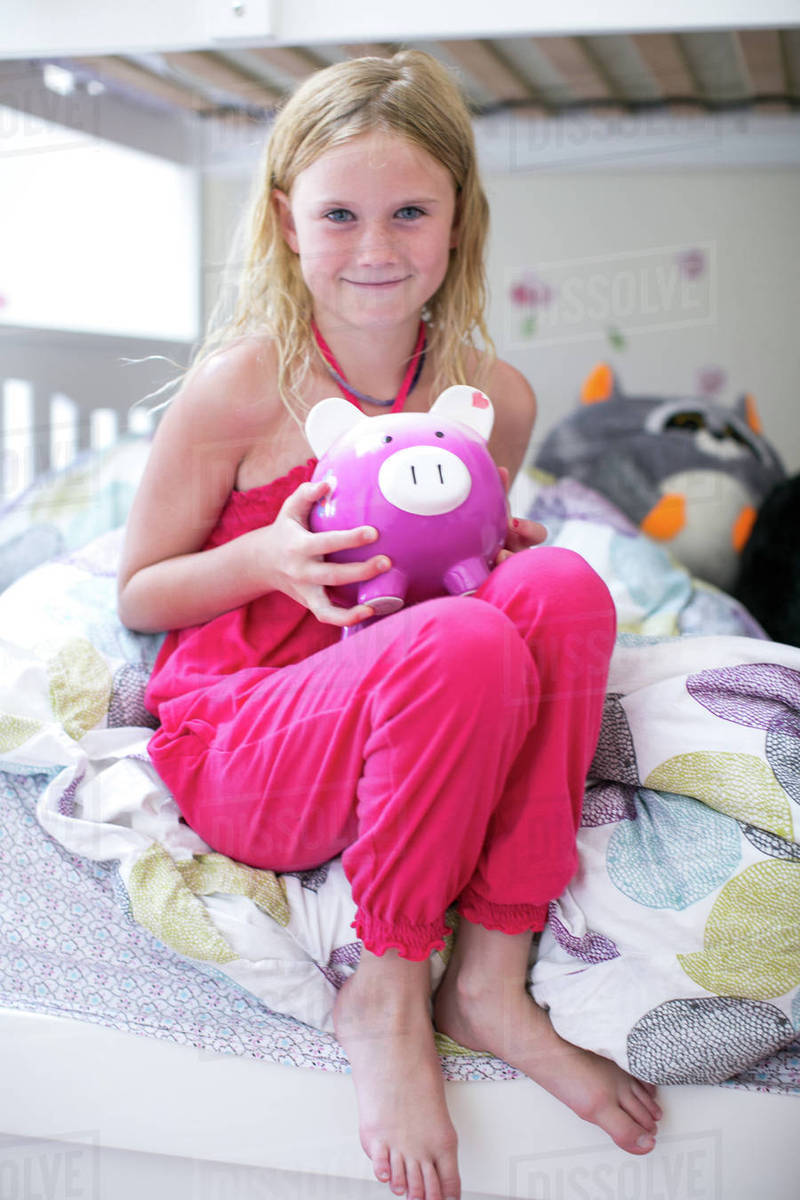 Portrait of girl sitting on bunk bed holding piggy bank Stock Photo