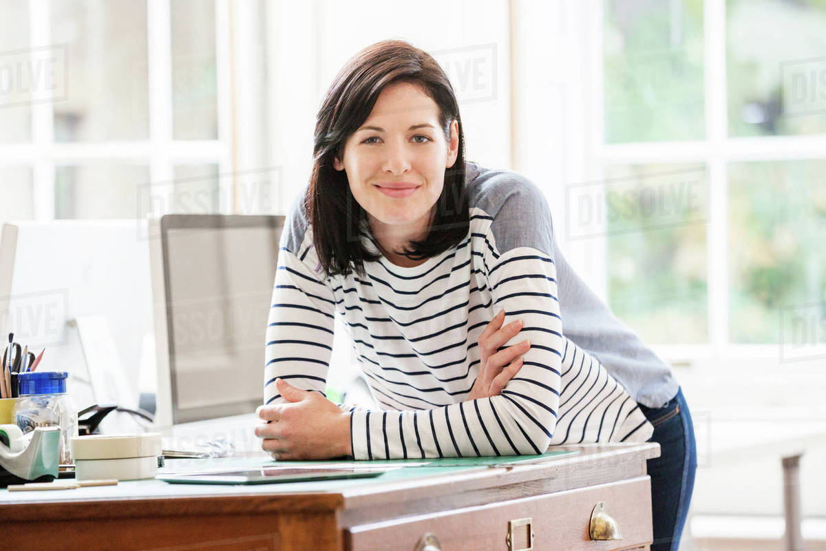 Portrait of female designer leaning forward on drawers in creative studio Stock Photo Dissolve
