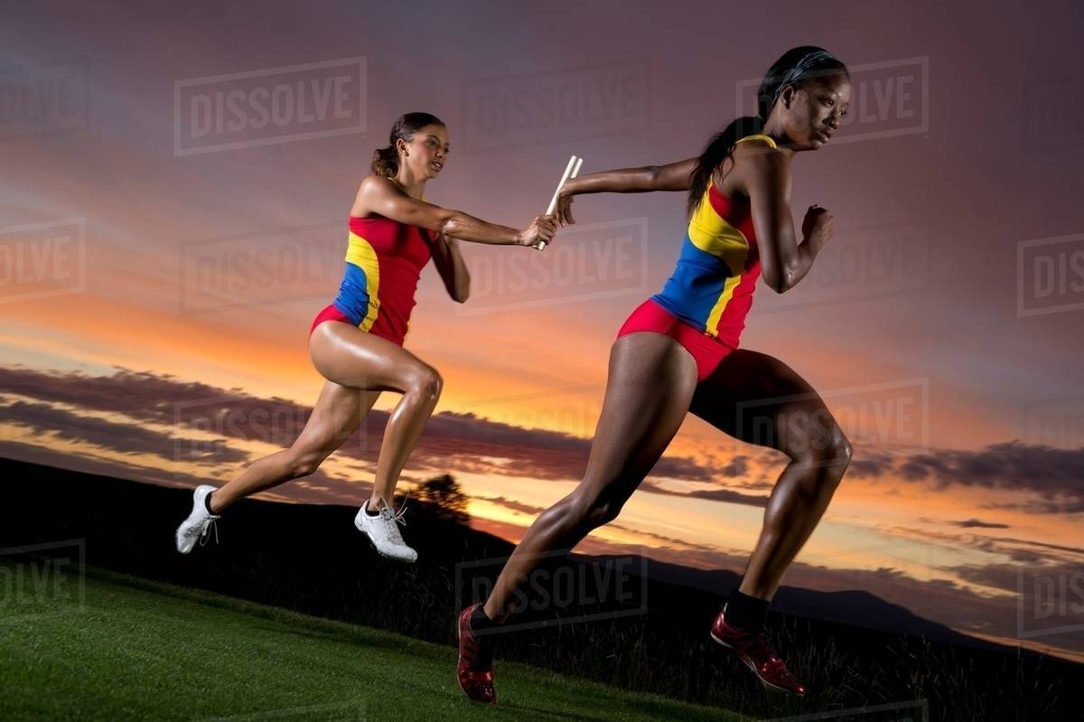 Female relay racers passing baton - Stock Photo - Dissolve