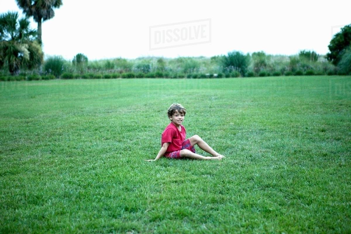Boy sitting in grassy field Stock Photo Dissolve