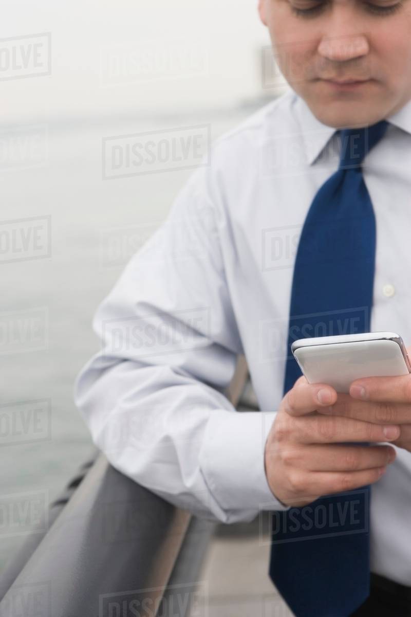 Businessman leaning on rail texting - Stock Photo - Dissolve