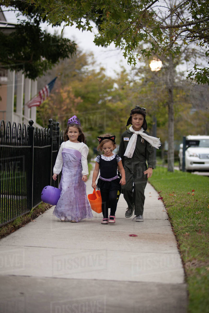 Boy and sisters walking along sidewalk trick or treating Royalty-free stock photo