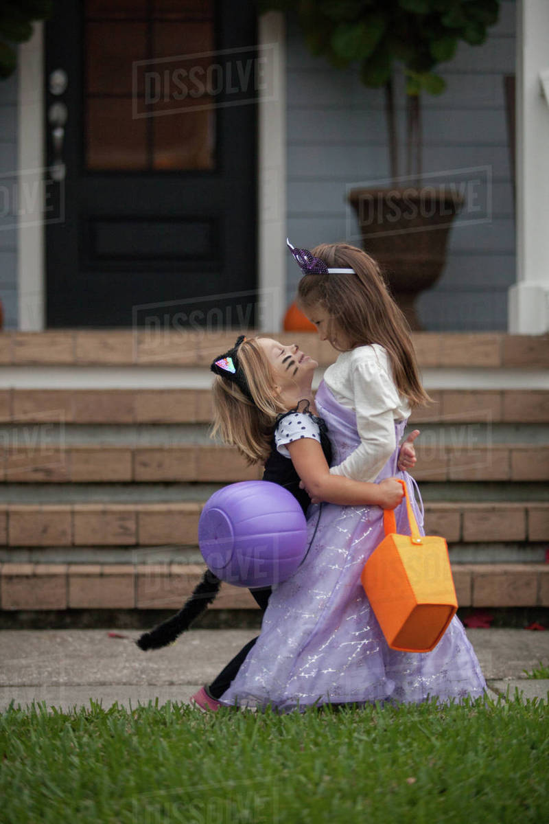 Two sisters trick or treating in cat and fairy costumes hugging at porch stairway Royalty-free stock photo