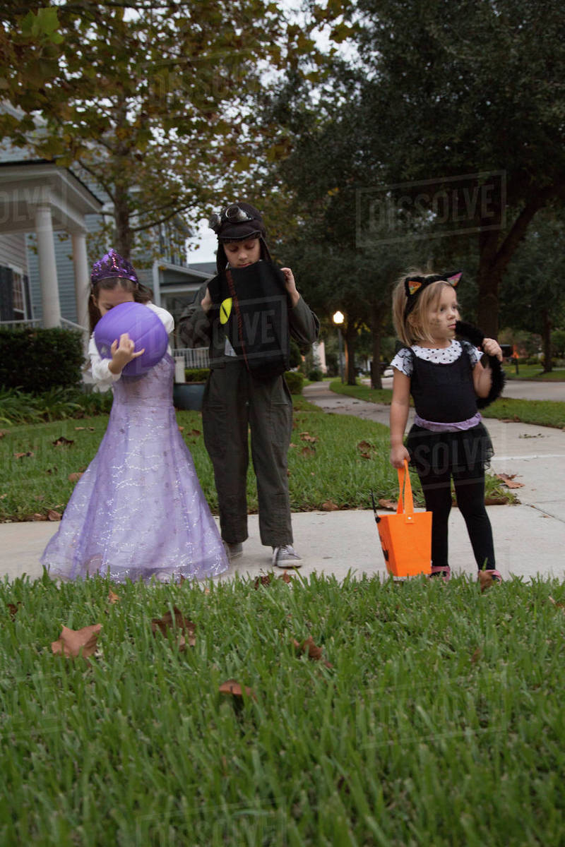Boy and sisters trick or treating looking in bags on sidewalk Royalty-free stock photo