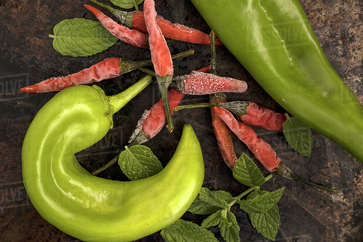An overhead shot of assorted peppers and peppermint leaves. Stock