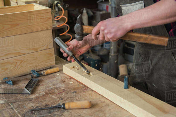 Carpenter working with a chisel and hammer in a wooden workshop ...