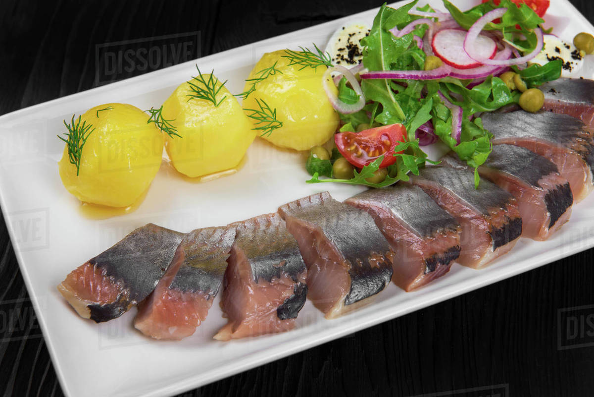 Sliced salted herring with vegetables on white plate Stock Photo