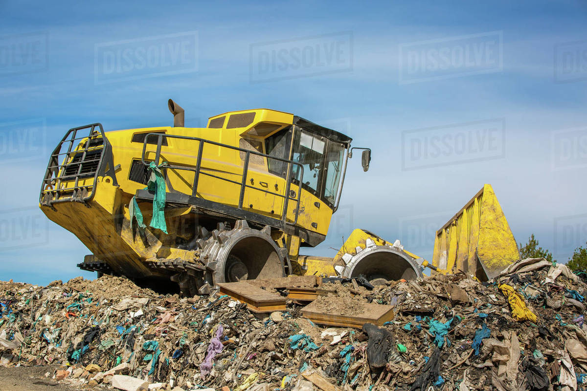 Huge bulldozer working at huge landfill or garbage dump, pollution ...