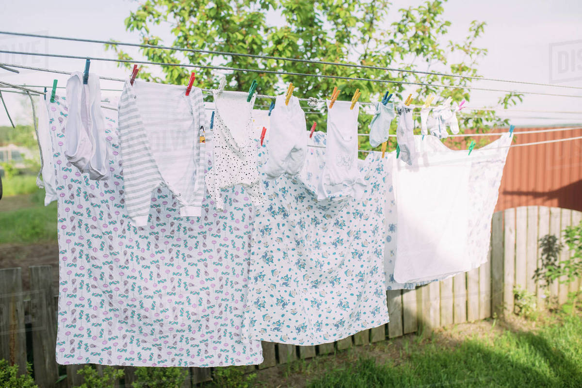 Clean washed newborn clothes are drying on a clothesline in the garden