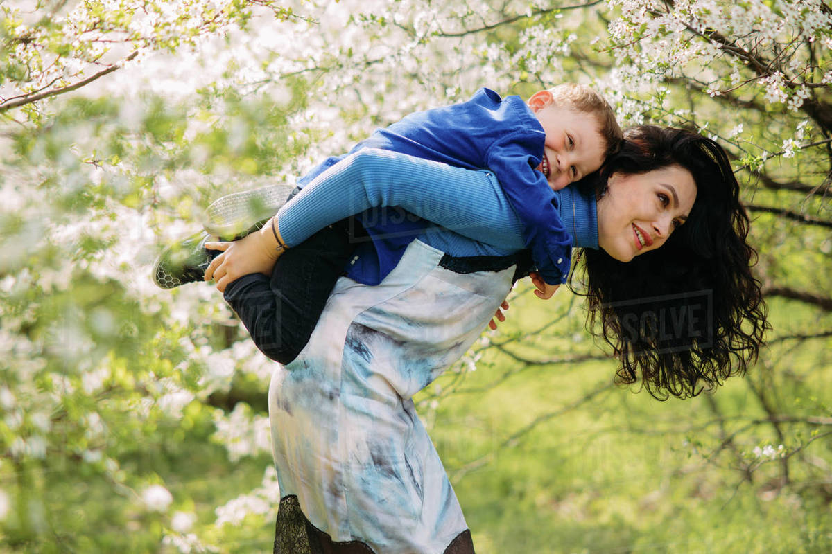 Happy mother and son play and have a fun on sunlit glade against background of blooming spring garden. Royalty-free stock photo