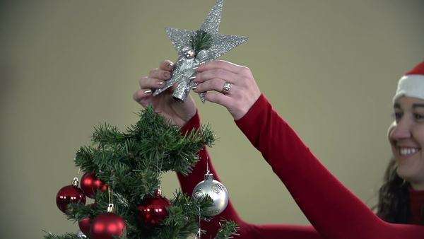 Young Romantic Couple Decorating Christmas Tree By A Fireplace
