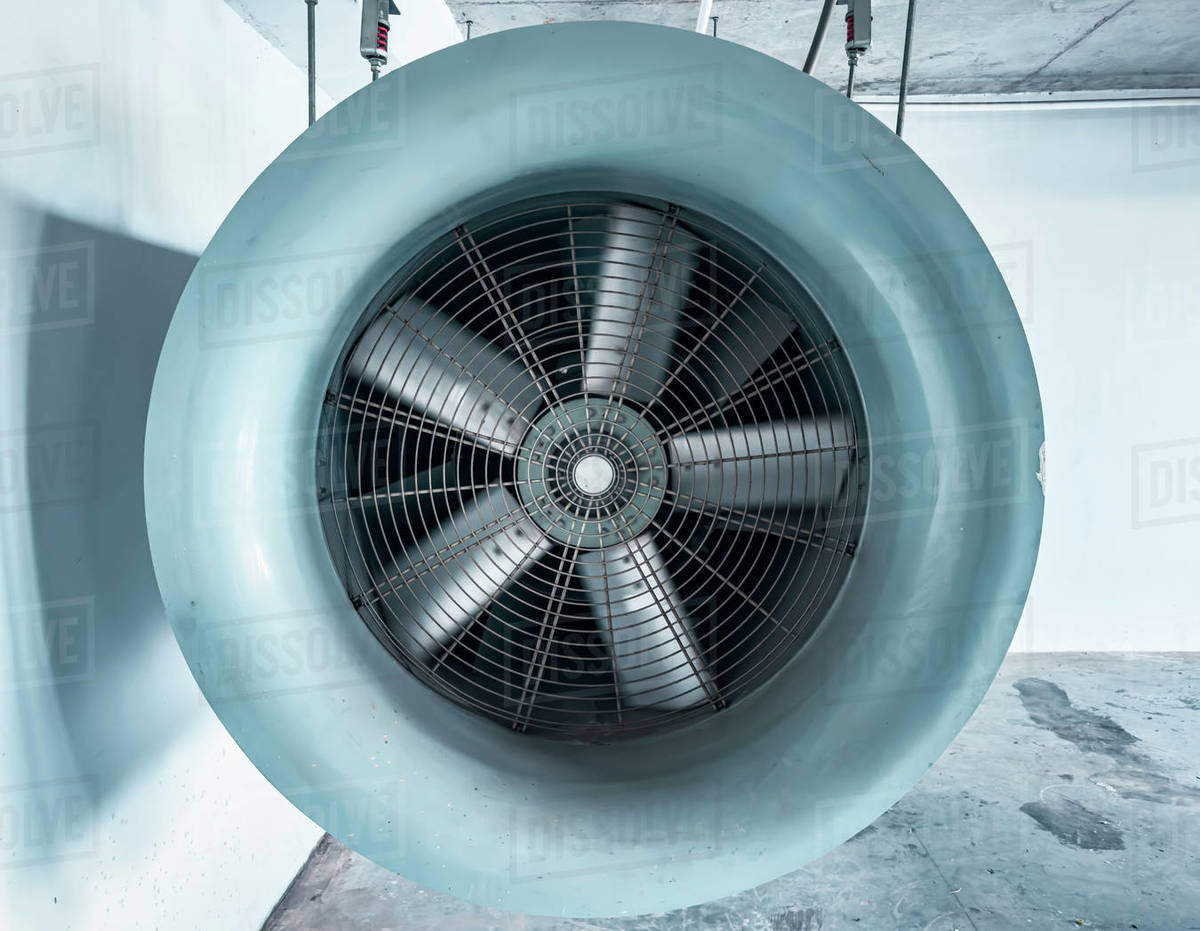 A large, gray, industrial fan is suspended from the ceiling of a ...