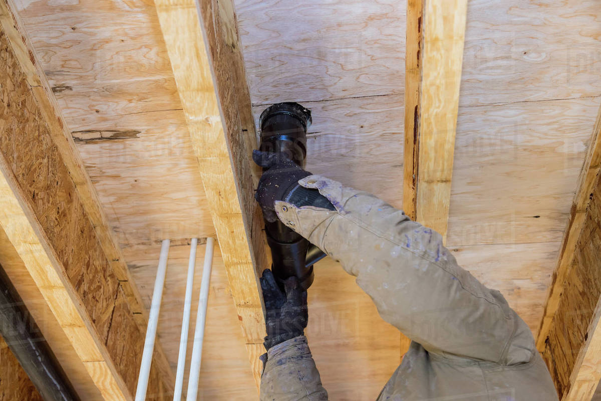 Plumber gluing cement CPVC plastic sewage drain pipe on of new house an