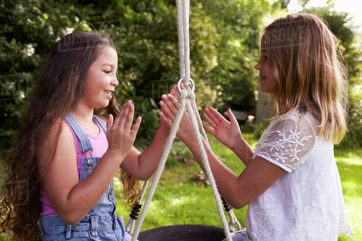 Two girls sitting on swing playing clapping game Stock Photo Dissolve