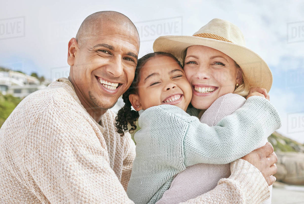 Mom, dad and child hug at the beach on family vacation, holiday