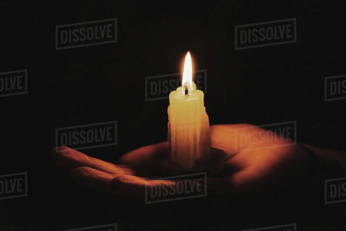 Burning candle on a female hand, dark background. Symbol of life