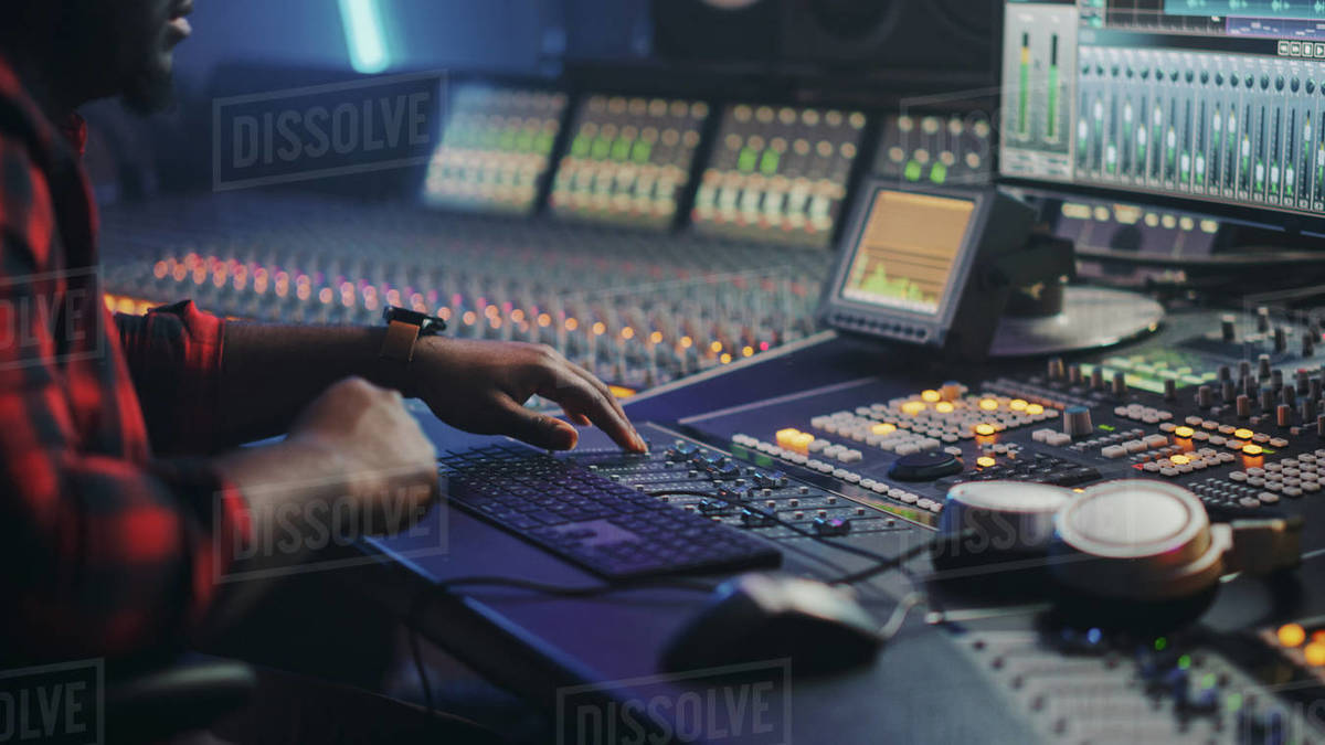 Energetic Male Audio Engineer Producer Working In Music Recording Studio Mixing Tracks On Control Desk And Software To Create Hit Song Track Artist Musician Enter His Studio At Sits At Workdesk