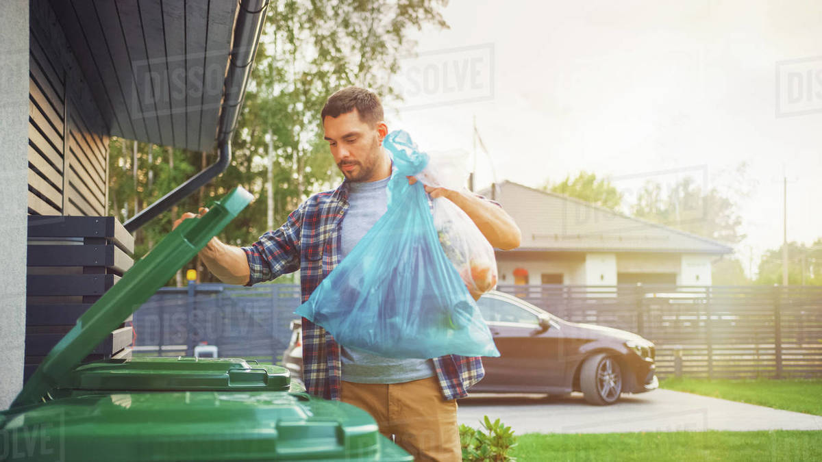 Man throwing away trash next to his house Stock Photo Dissolve