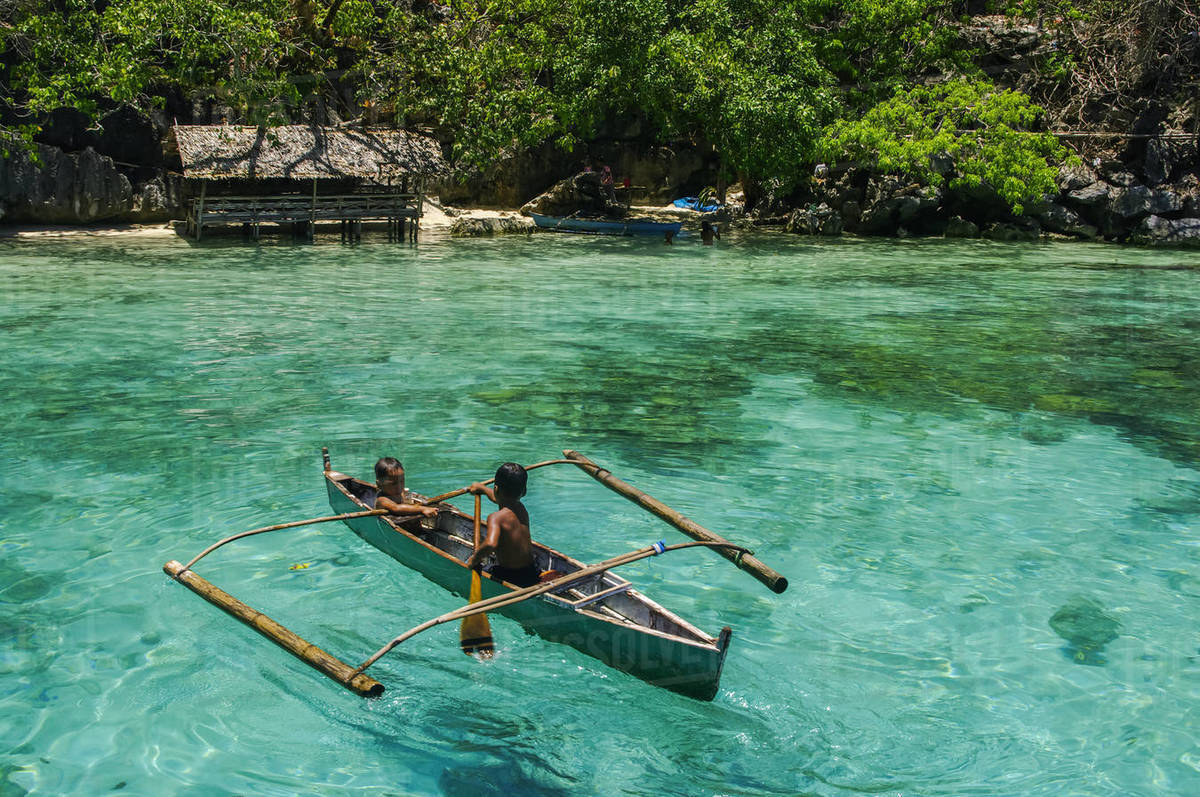 Boys paddling in an outrigger canoe, fishing in the turquoise waters of