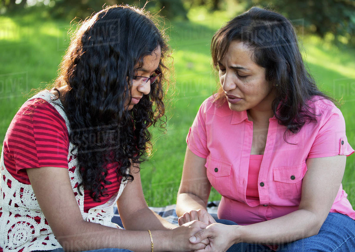 Mother and daughter praying together in a park; Edmonton, Alberta