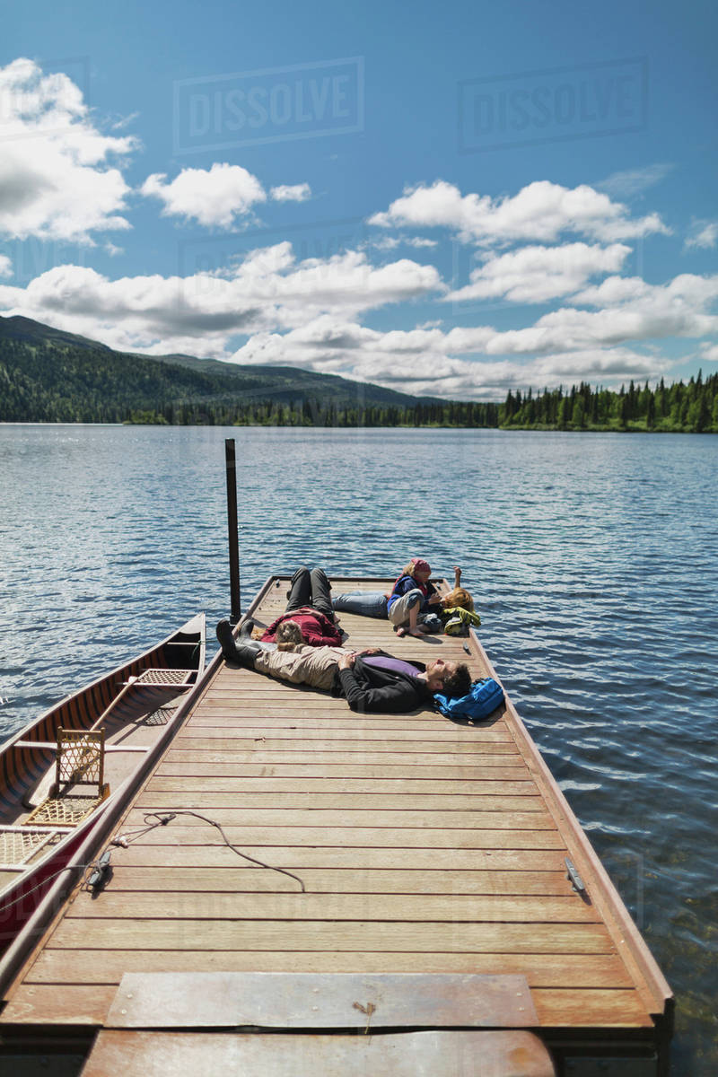 Three adults and a young girl lounging on a boat dock on a lake soaking