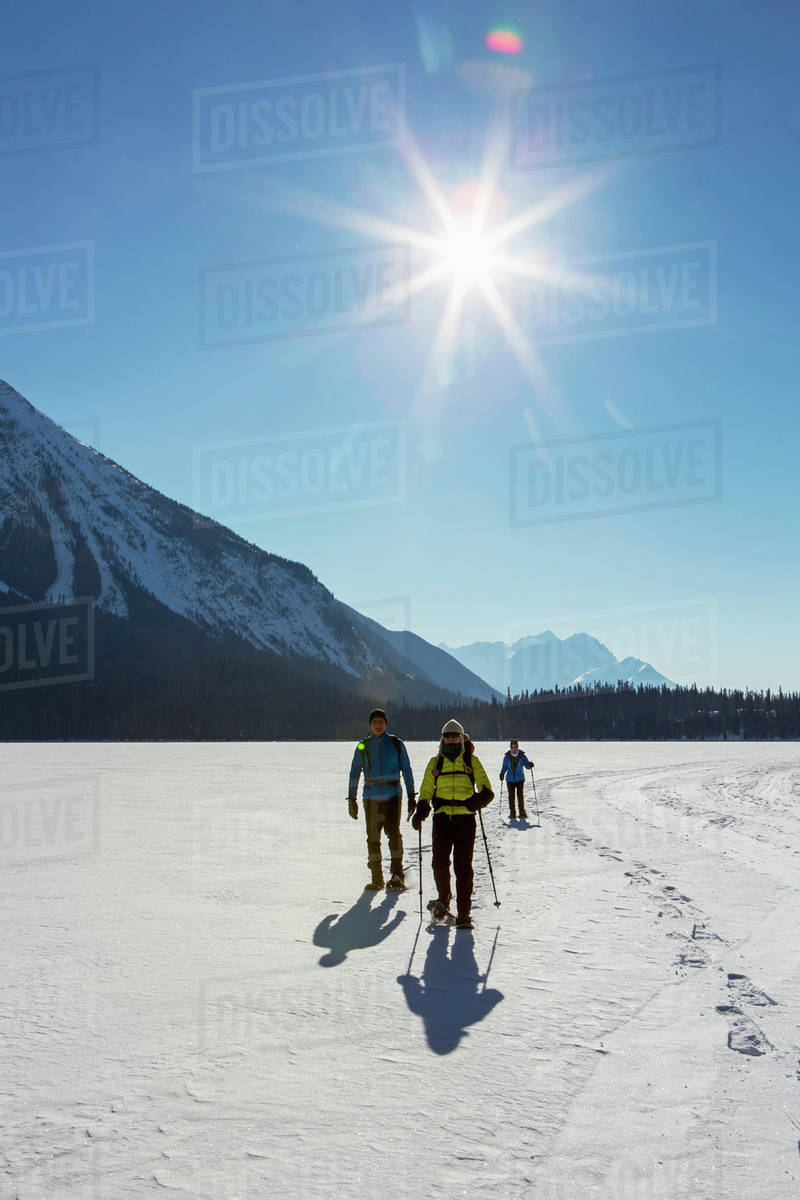 Group snowshoeing on snow covered mountain lake with sunburst and blue