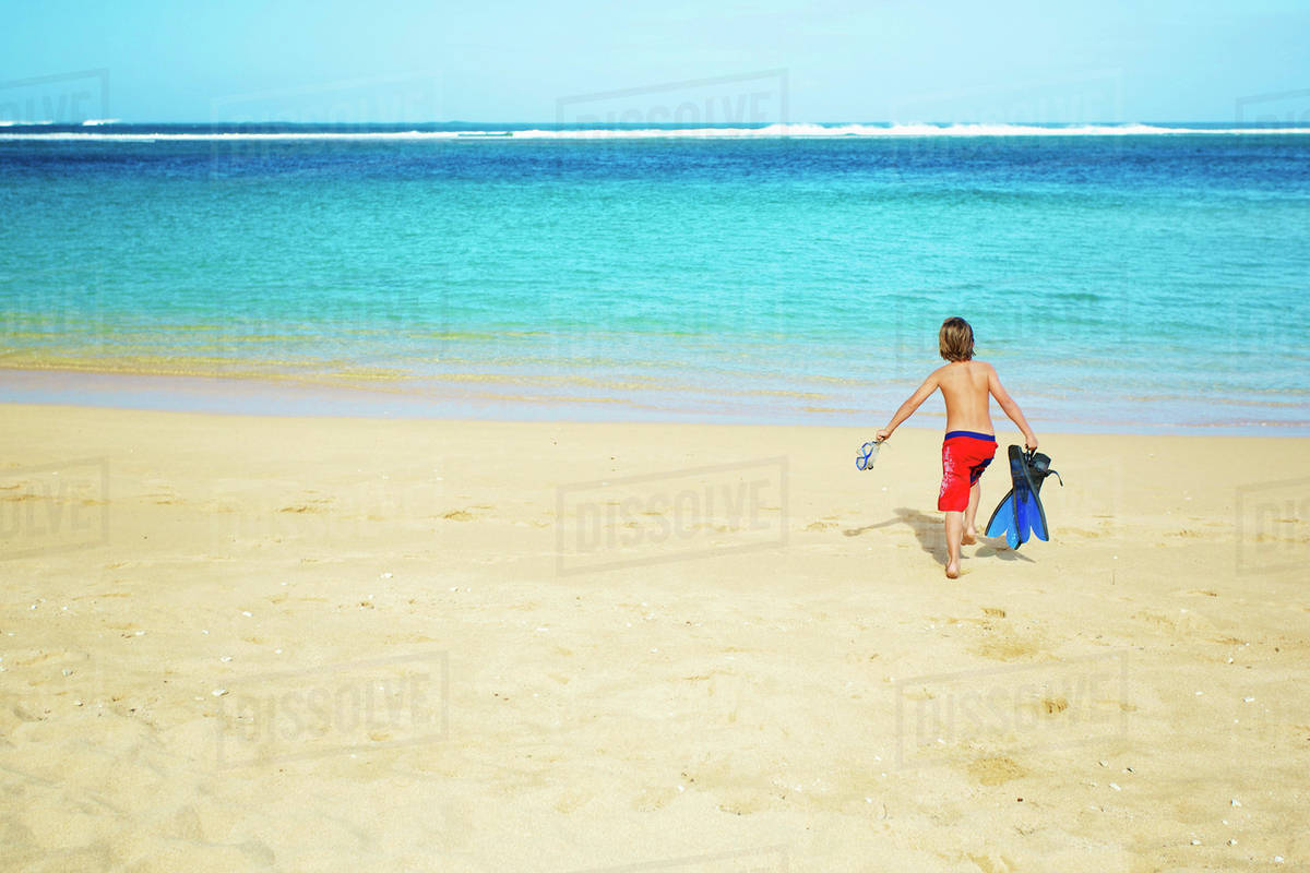 A boy running out to the ocean across the beach with snorkelling gear