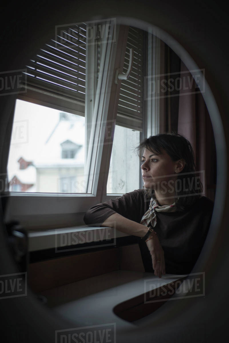 Reflection in a mirror of a woman sitting and looking out the window ...