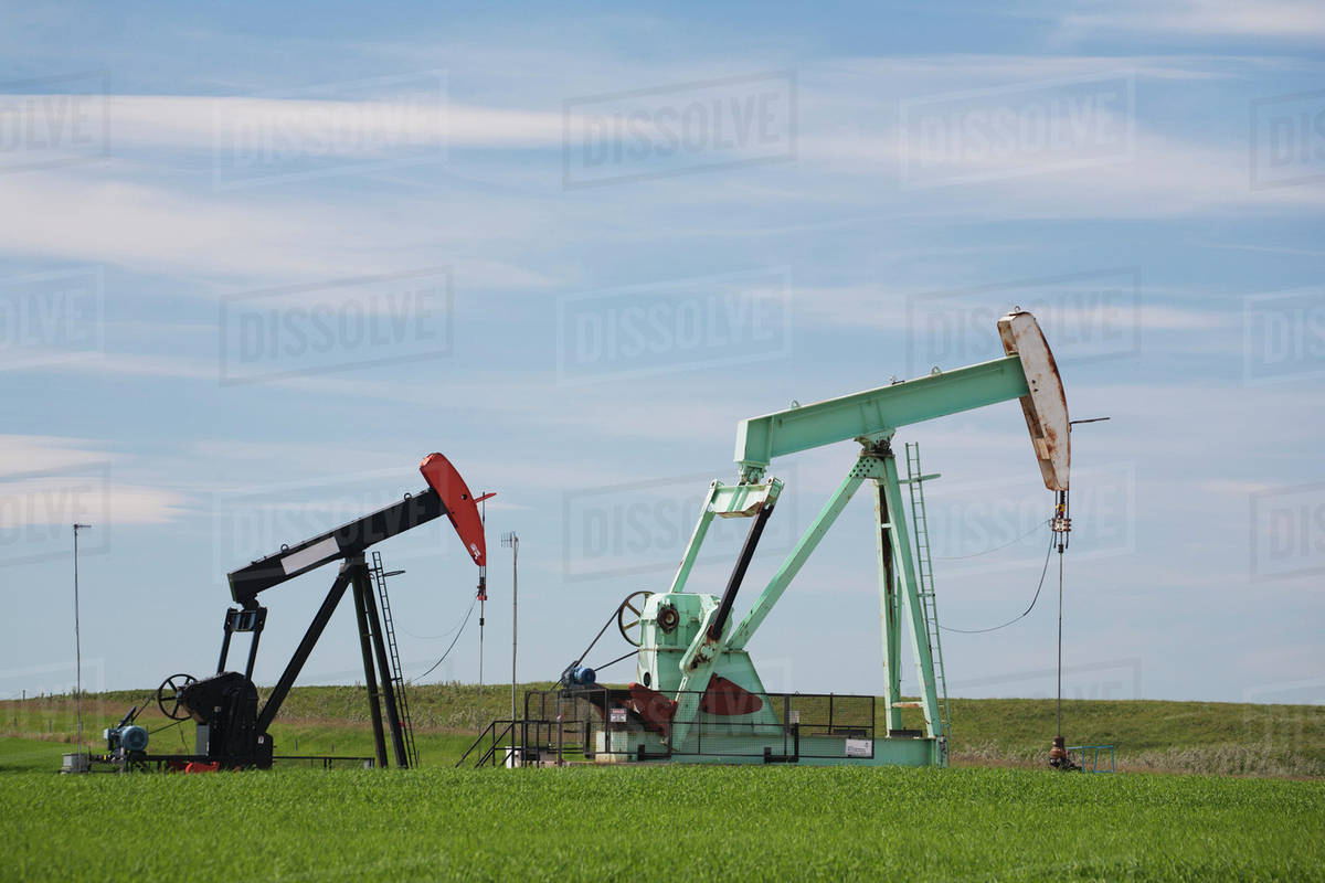 Two pump jacks in a field with clouds and blue sky east of airdrie