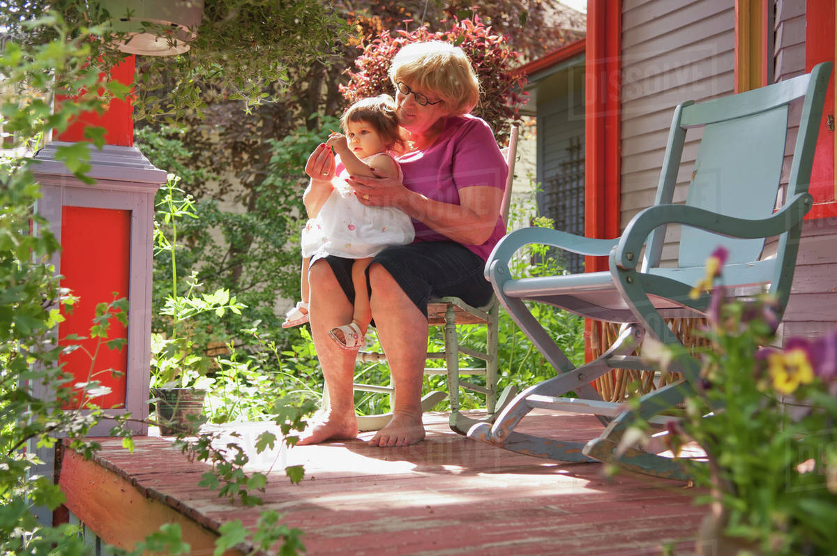Grandmother And Child Sitting On Front Porch With Many Plants