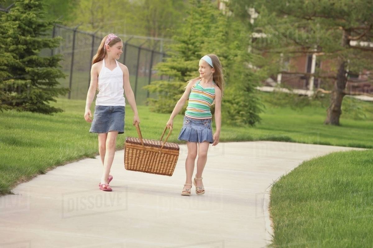 Edmonton, Alberta, Canada; Two Girls Carrying A Picnic Basket Down The