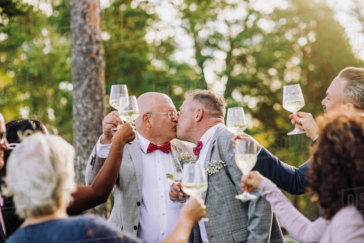 Newlywed gay couple kissing each other while raising toast amidst