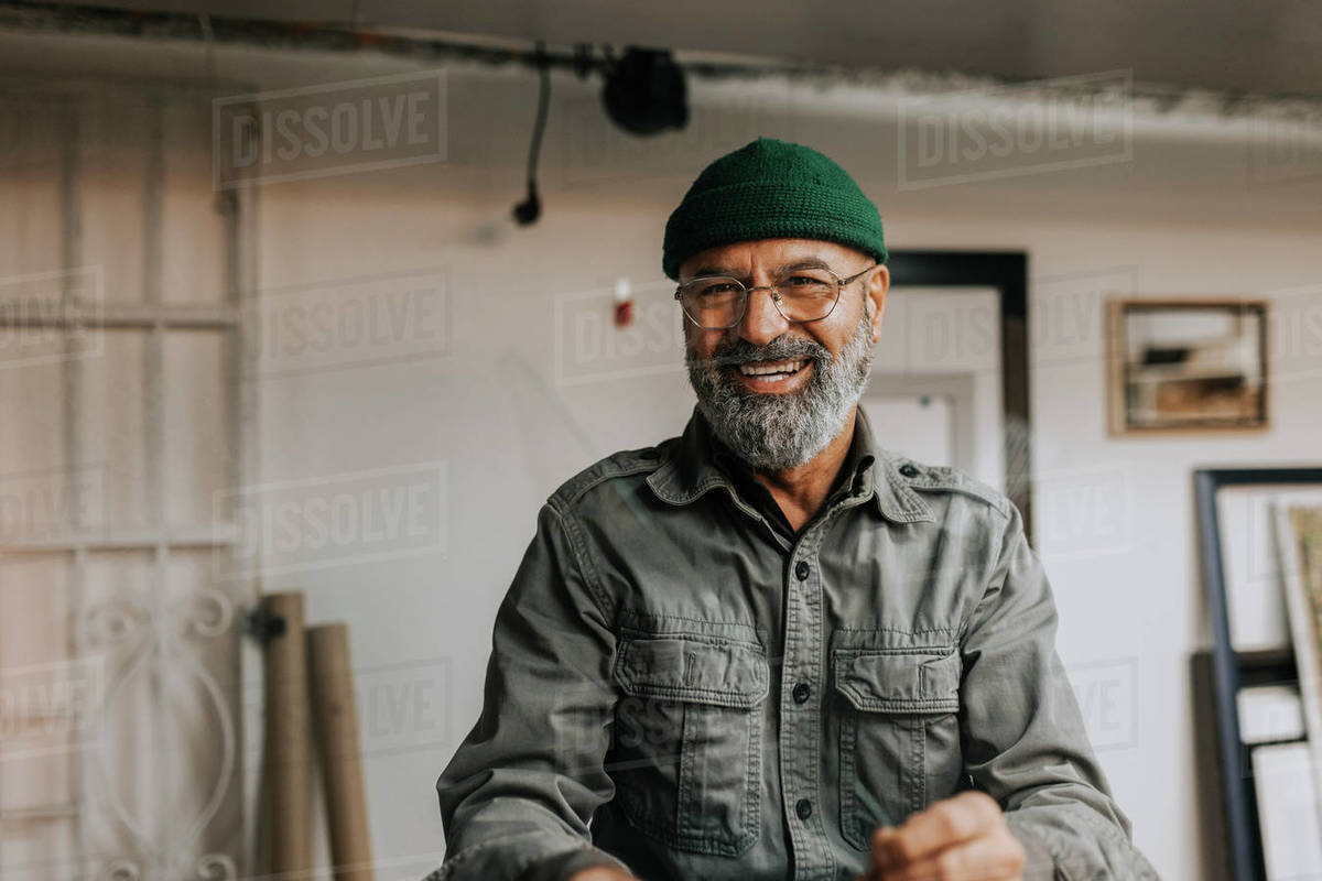 Portrait of cheerful male owner wearing knit hat and eyeglasses in
