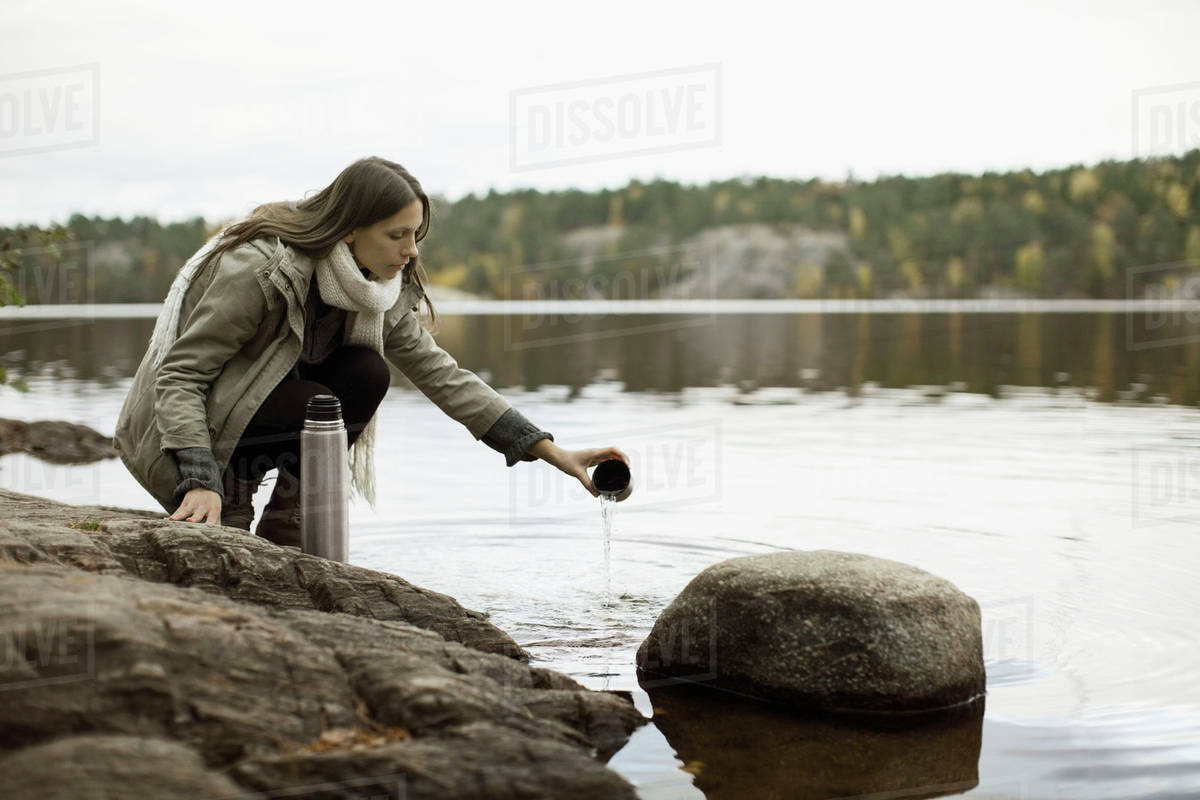 Woman washing thermos at lakeshore Stock Photo Dissolve