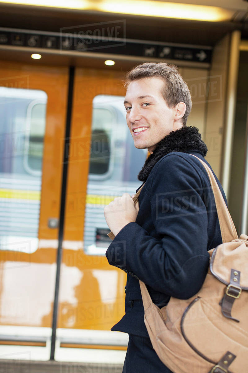Portrait of smiling young businessman with backpack on railroad station