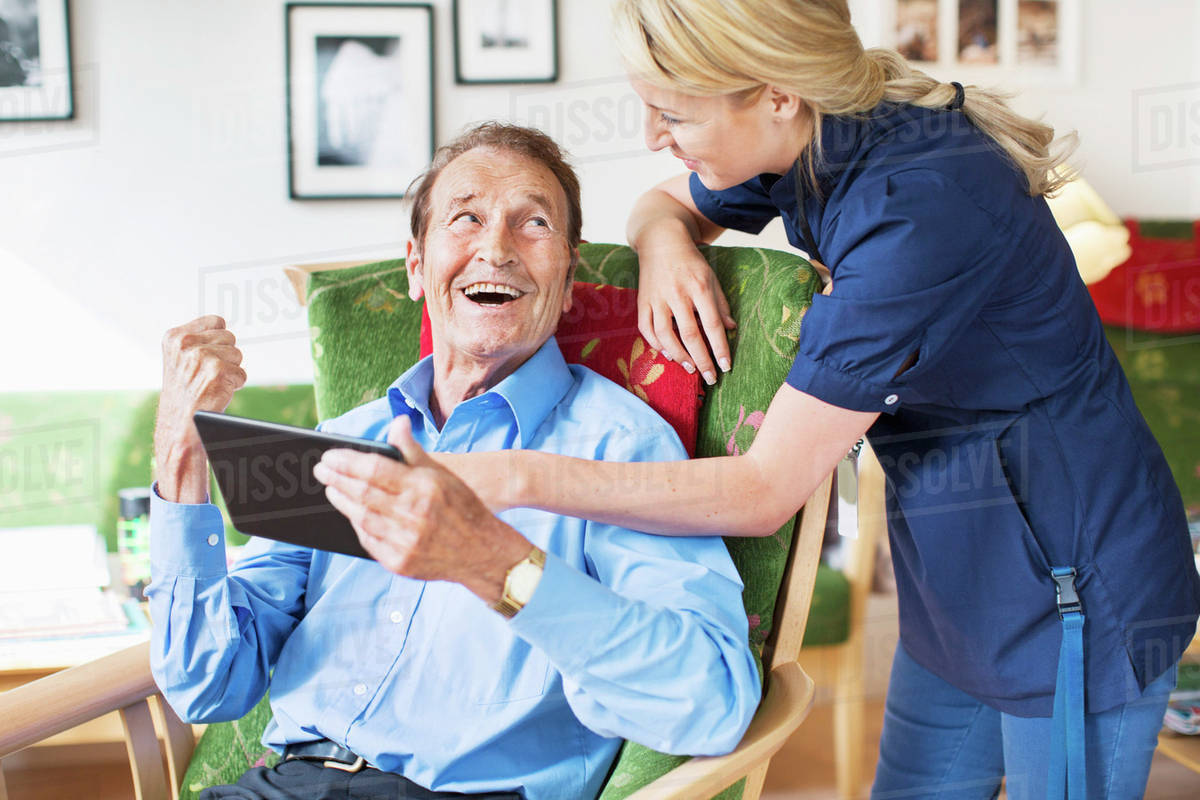 Happy senior man and female caretaker using digital tablet at nursing home Royalty-free stock photo