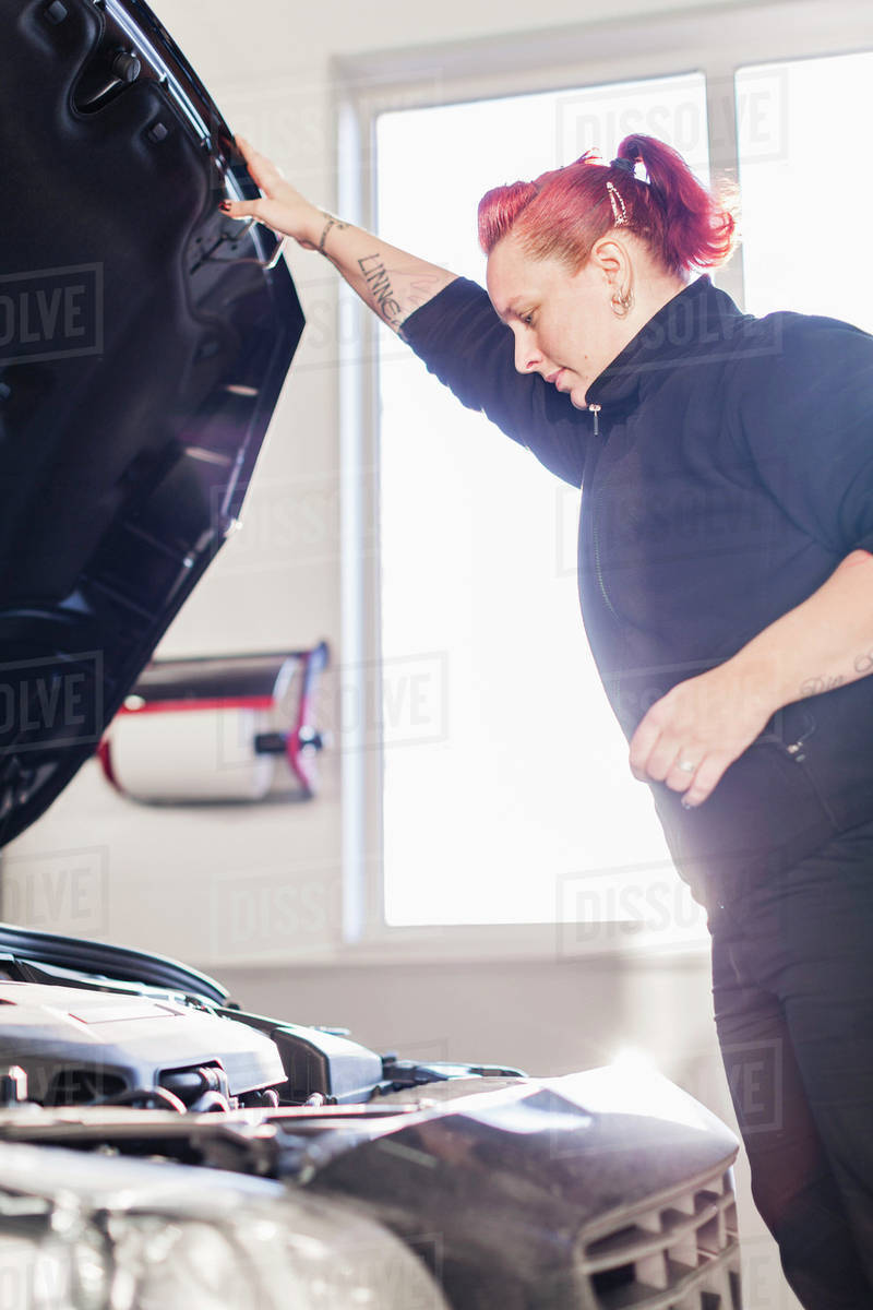 Female mechanic opening car's hood in auto repair shop Stock Photo