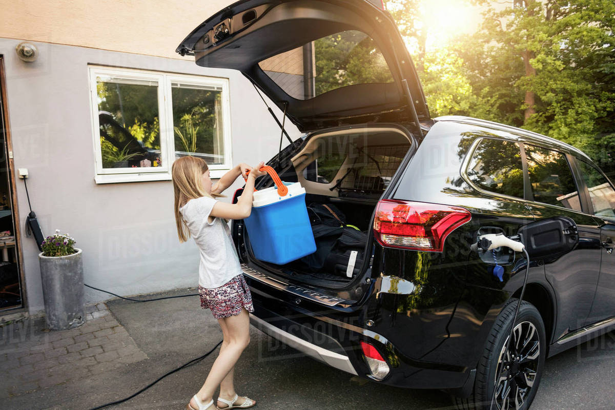 Girl loading cooler in black car trunk against house Royalty-free stock photo