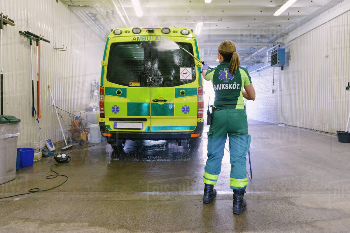 Rear view of female paramedic washing ambulance at parking lot Stock